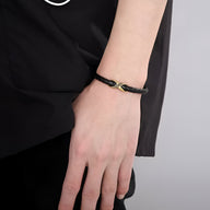 Bracelet en cuir noir tressé avec nœud central en acier doré sur poignet masculin.