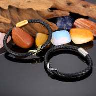 Bracelet en cuir noir tressé avec nœud central en acier doré et argenté posé sur fond noir avec pierres colorées.