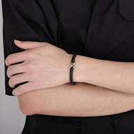 Bracelet en cuir noir avec nœud central en acier doré, design élégant pour homme.