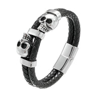 Bracelet en cuir noir tressé avec ornement double têtes de mort en métal argenté et fermoir magnétique.