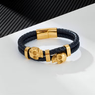 Bracelet en cuir noir tressé avec ornement double têtes de mort dorées et fermoir magnétique doré.