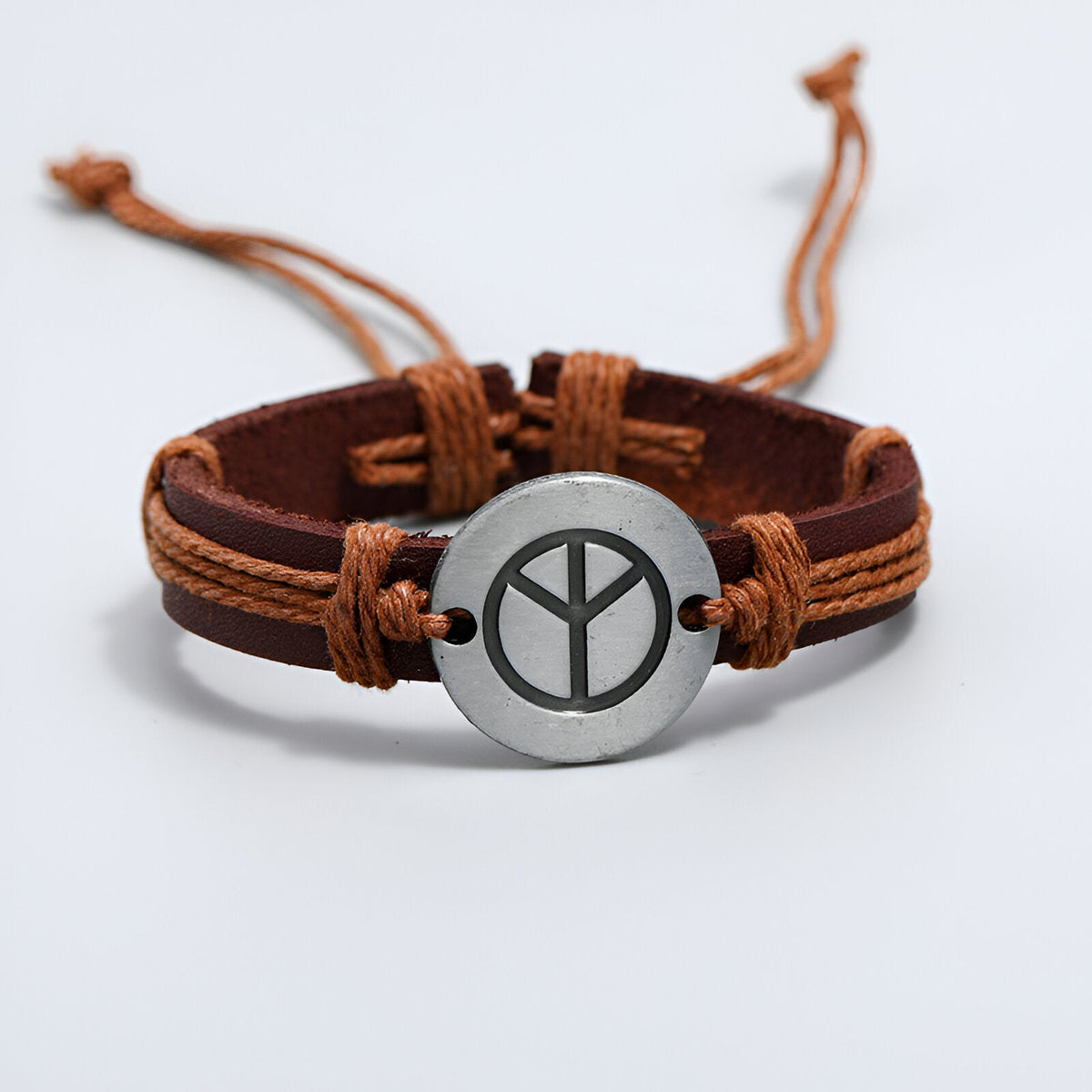 Bracelet en cuir marron avec médaille ronde en métal gravée du symbole de la paix, lacets réglables en corde beige.