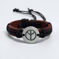 Bracelet en cuir marron à double lanière avec pendentif rond en métal argenté arborant un symbole de paix noir.