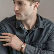 Bracelet en cuir noir avec trois plaques métalliques gravées porté au poignet d’un homme habillé d’une chemise en jean noire.