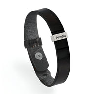 Bracelet en cuir noir avec plaque métallique gravée et fermoir à bouton-pression.