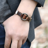 Bracelet homme en cuir marron avec anneau métallique rond et fermeture à boucle.