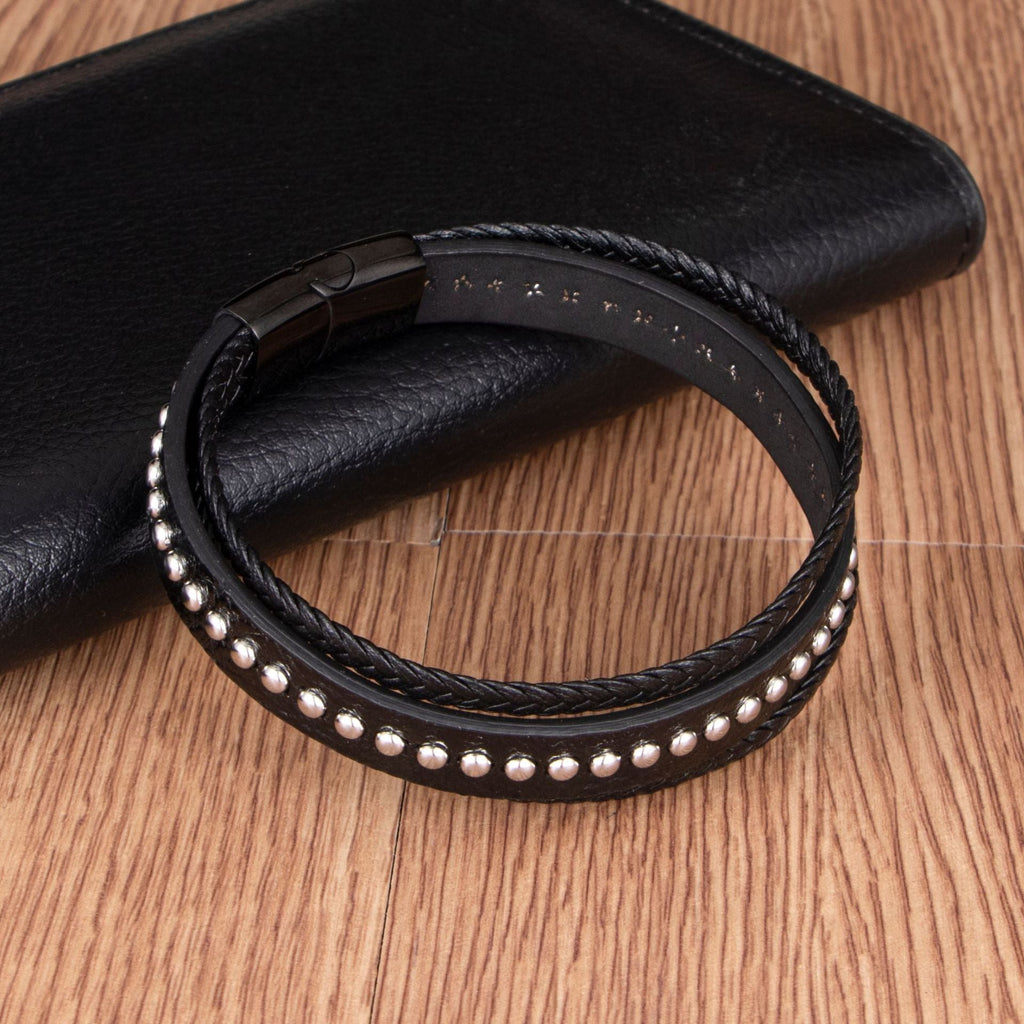 Bracelet multi-rangs en cuir noir avec rivets métalliques et fermeture magnétique.