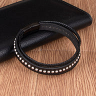 Bracelet multi-rangs en cuir noir avec rivets métalliques et fermeture magnétique.