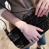 Bracelet fin en cuivre plaqué or avec pendentif trèfle à 4 feuilles porté au poignet féminin.