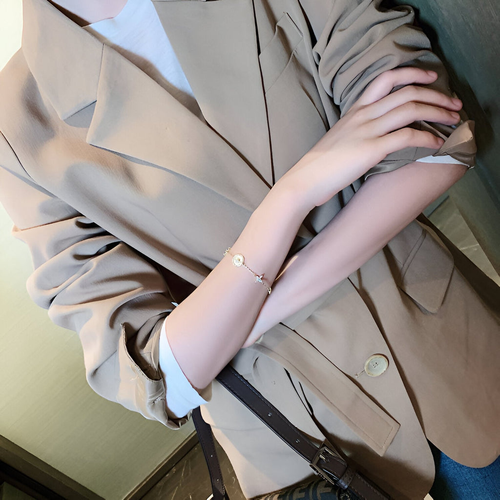 Bracelet fin en cuivre plaqué or avec pendentif trèfle à 4 feuilles porté au poignet féminin.