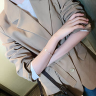 Bracelet fin en cuivre plaqué or avec pendentif trèfle à 4 feuilles porté au poignet féminin.