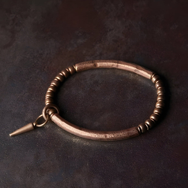 Bracelet en cuivre marron avec pendentif conique et perles rondes, style raffiné et minimaliste.