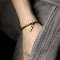 Bracelet fin en cuivre marron avec pendentif clé minimaliste sur poignet féminin.