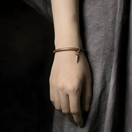 Bracelet en cuivre fin avec pendentif petit anneau, style minimaliste, porté au poignet marron.