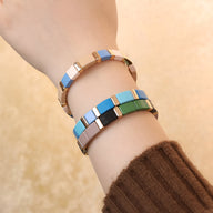 Bracelet émail coloré multicolore aux tons bleu, vert et beige sur poignet féminin.