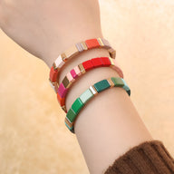 Bracelets en émail multicolores style Calypso, avec sections rectangulaires et détails dorés, portés au poignet féminin.