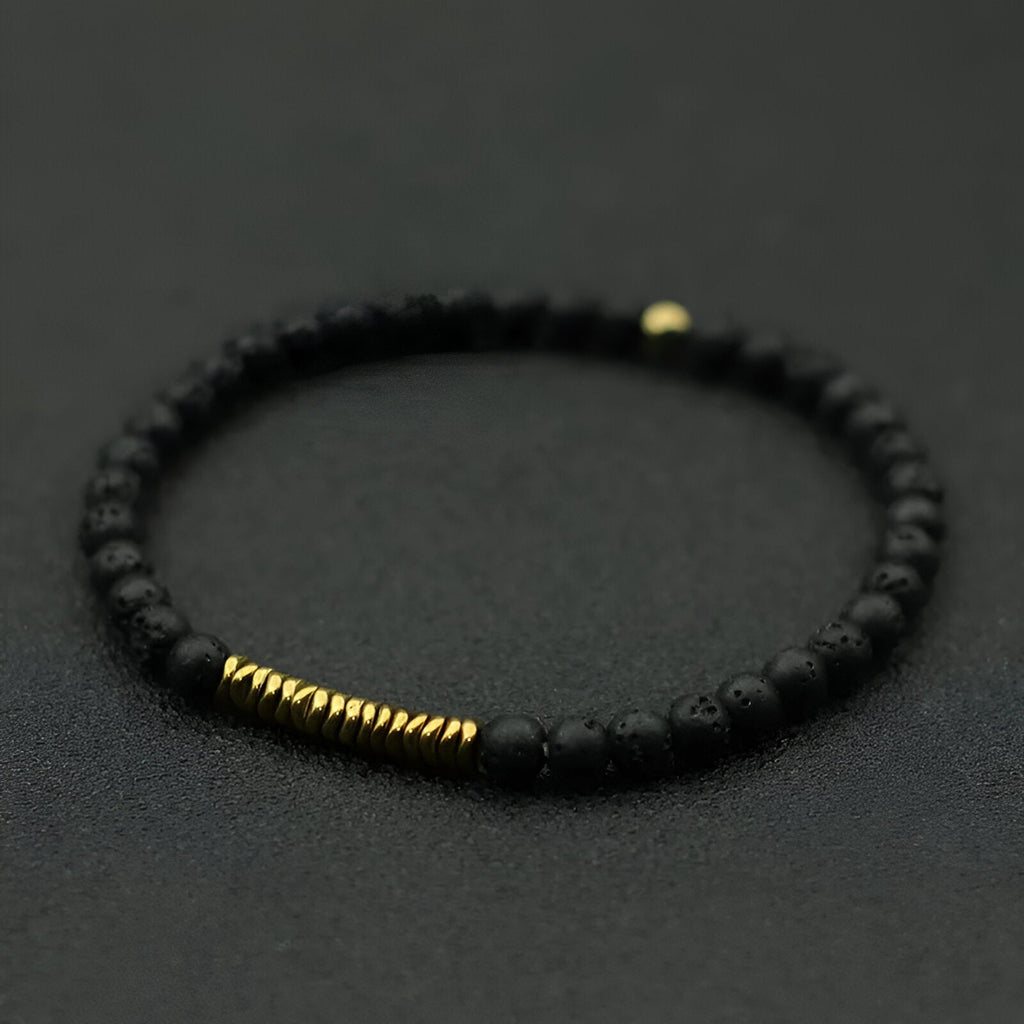Bracelet fin pour homme en pierres volcaniques noires mates avec petits anneaux dorés.
