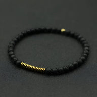 Bracelet fin pour homme en pierres volcaniques noires mates avec petits anneaux dorés.