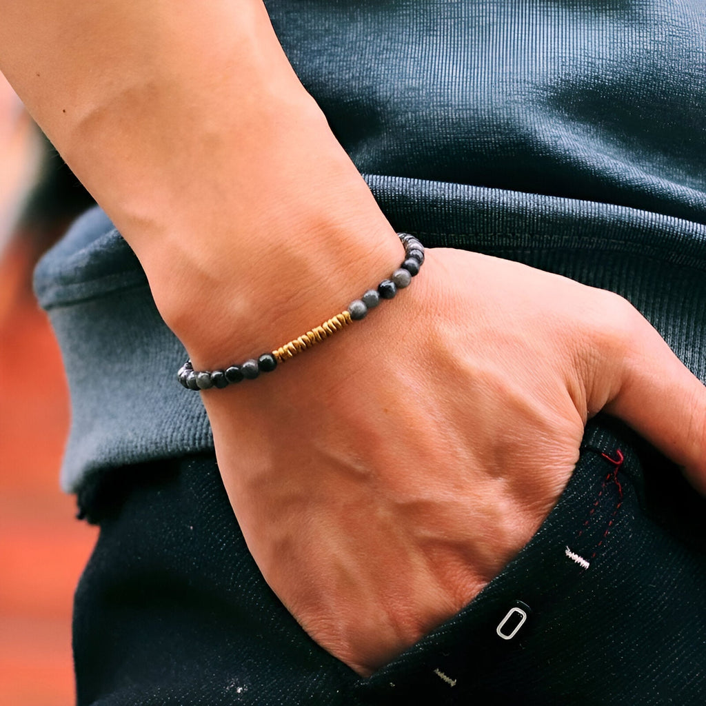 Bracelet fin en hématite noire et perles dorées sur poignet masculin, style moderne et épuré.