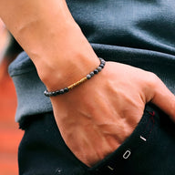 Bracelet fin en hématite noire et perles dorées sur poignet masculin, style moderne et épuré.