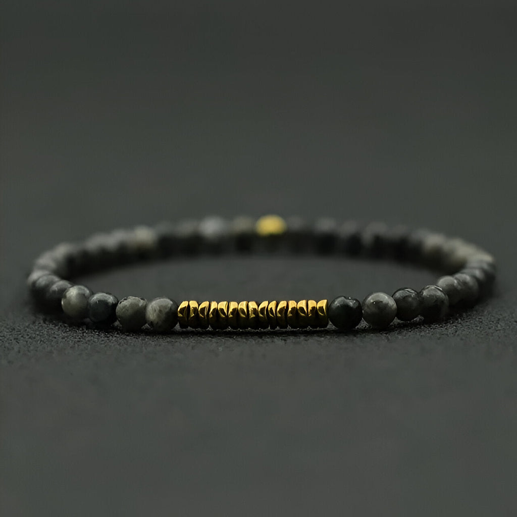 Bracelet fin pour homme en pierres noires mat et perles dorées au centre.