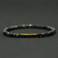Bracelet fin pour homme en pierres noires mat et perles dorées au centre.
