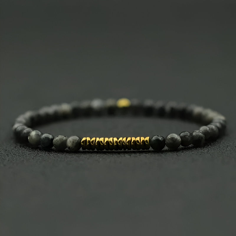 Bracelet fin pour homme en pierres noires mat et perles dorées au centre.