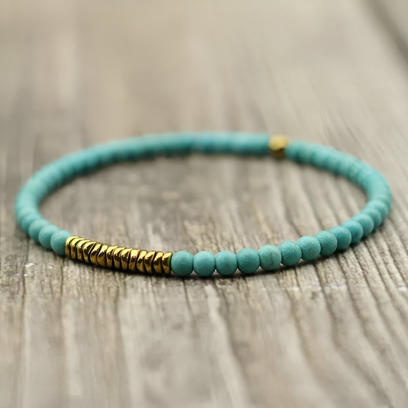 Bracelet fin en perles turquoise avec accents en hématite dorée sur corde élastique.