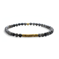 Bracelet fin en perles noires volcanique avec sections dorées, style masculin élégant.