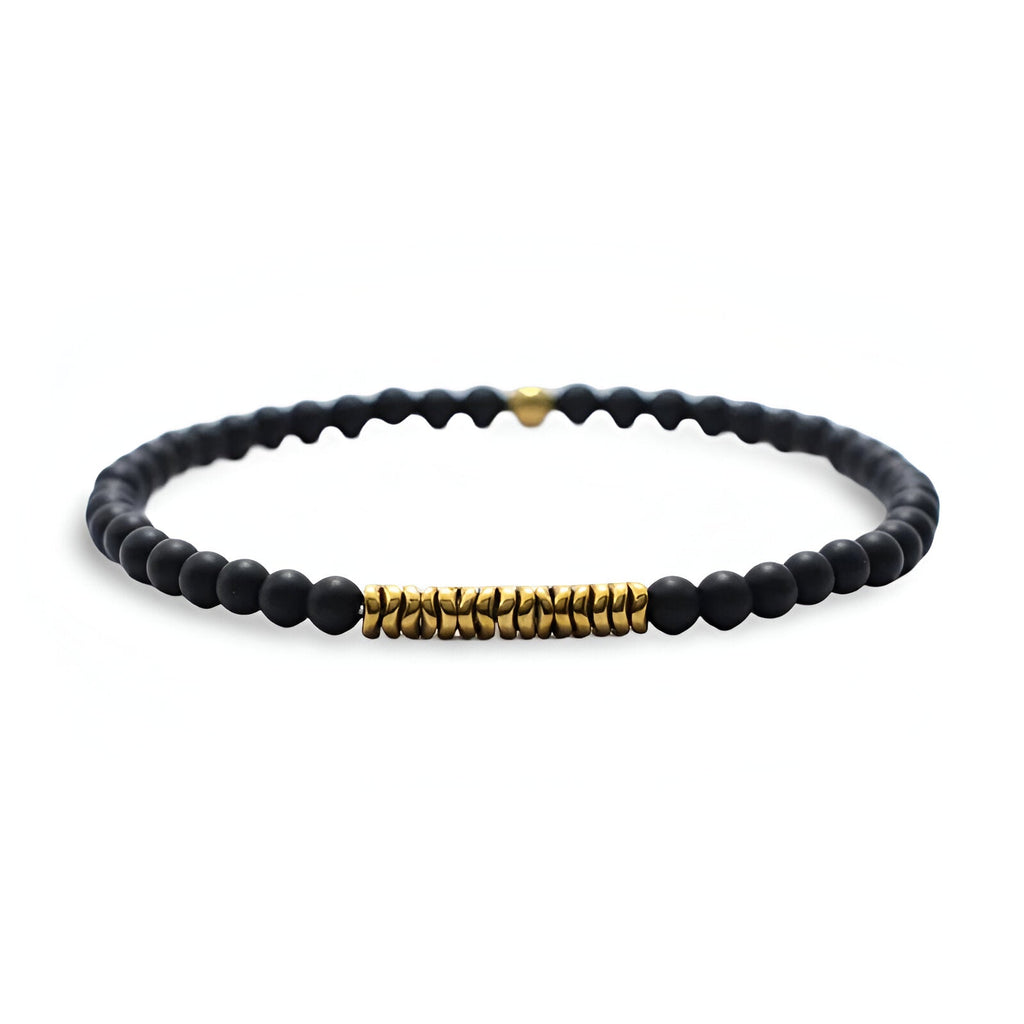 Bracelet fin pour homme en perles noires mates avec détails cylindriques dorés et petit cœur doré.