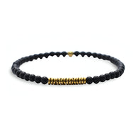 Bracelet fin pour homme en perles noires mates avec détails cylindriques dorés et petit cœur doré.