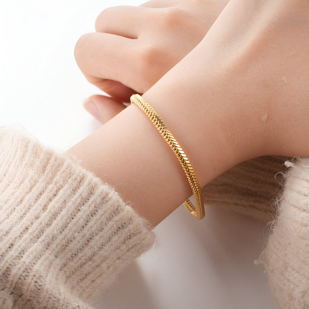 Bracelet jonc en maille serpent doré en acier inoxydable porté au poignet féminin.