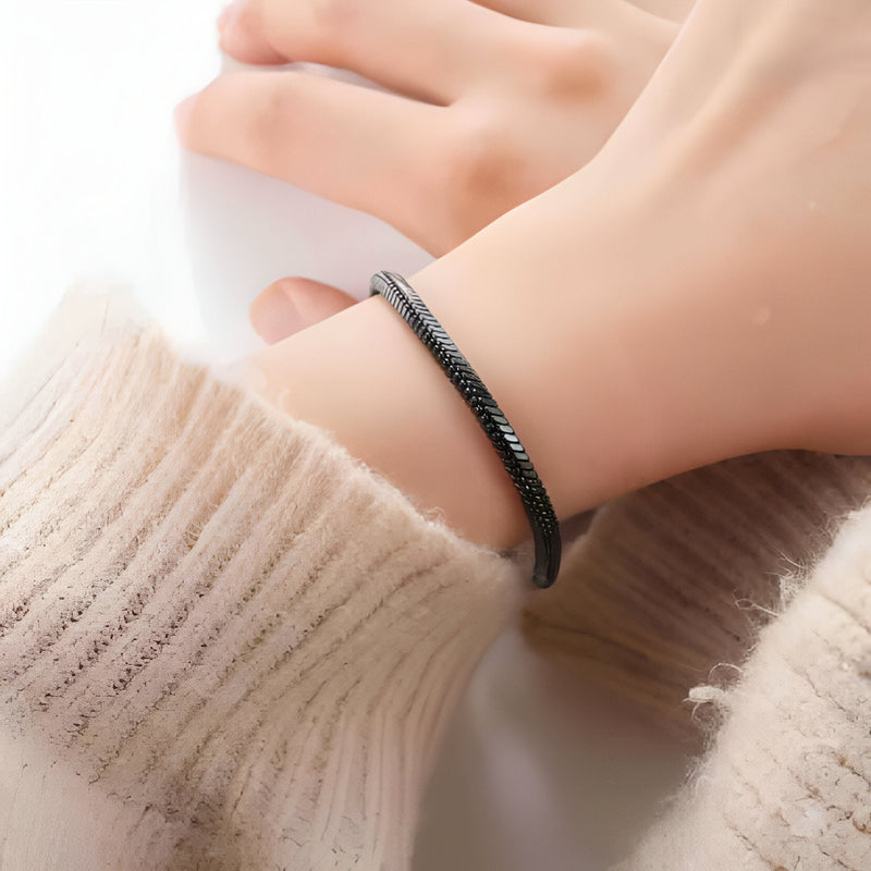 Bracelet jonc maille serpent noir en acier inoxydable porté au poignet féminin.