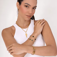 Bracelet jonc flexible en maille serpent doré en titane porté avec bagues et collier dorés sur peau claire.