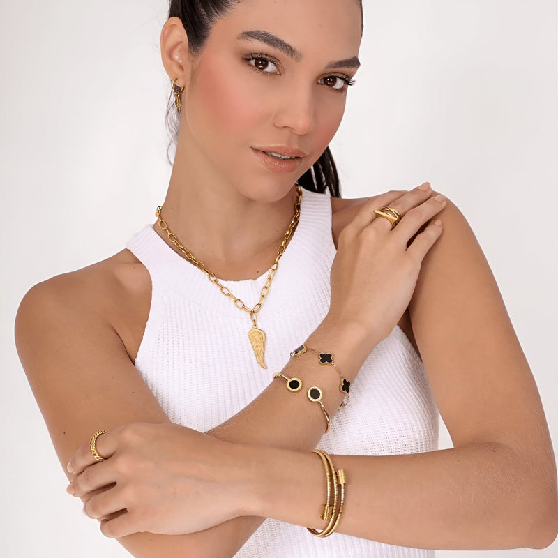 Bracelet jonc flexible en maille serpent doré en titane porté avec bagues et collier dorés sur peau claire.