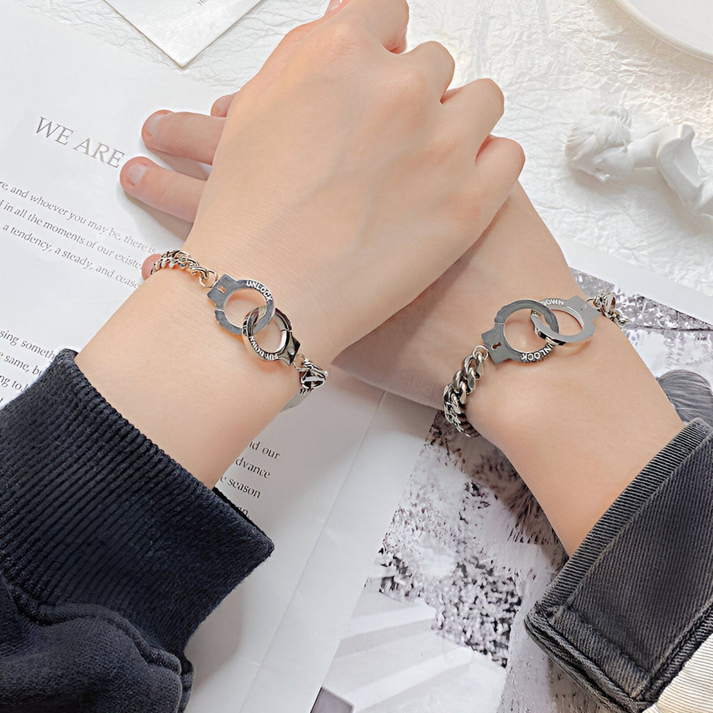 Bracelet en maille argentée avec menottes entrelacées en acier inoxydable porté sur poignet féminin.