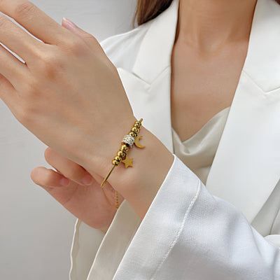 Bracelet serpent doré en acier inoxydable avec pendentif lune et étoiles sur poignet féminin.