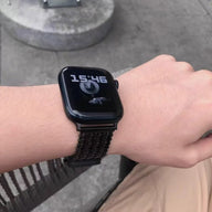 Bracelet de montre Apple en maille V épaisse noire, ajustable et robuste, porté au poignet.