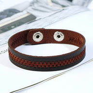 Bracelet marron en microfibre avec tressage central et fermeture à pressions métalliques argentées.