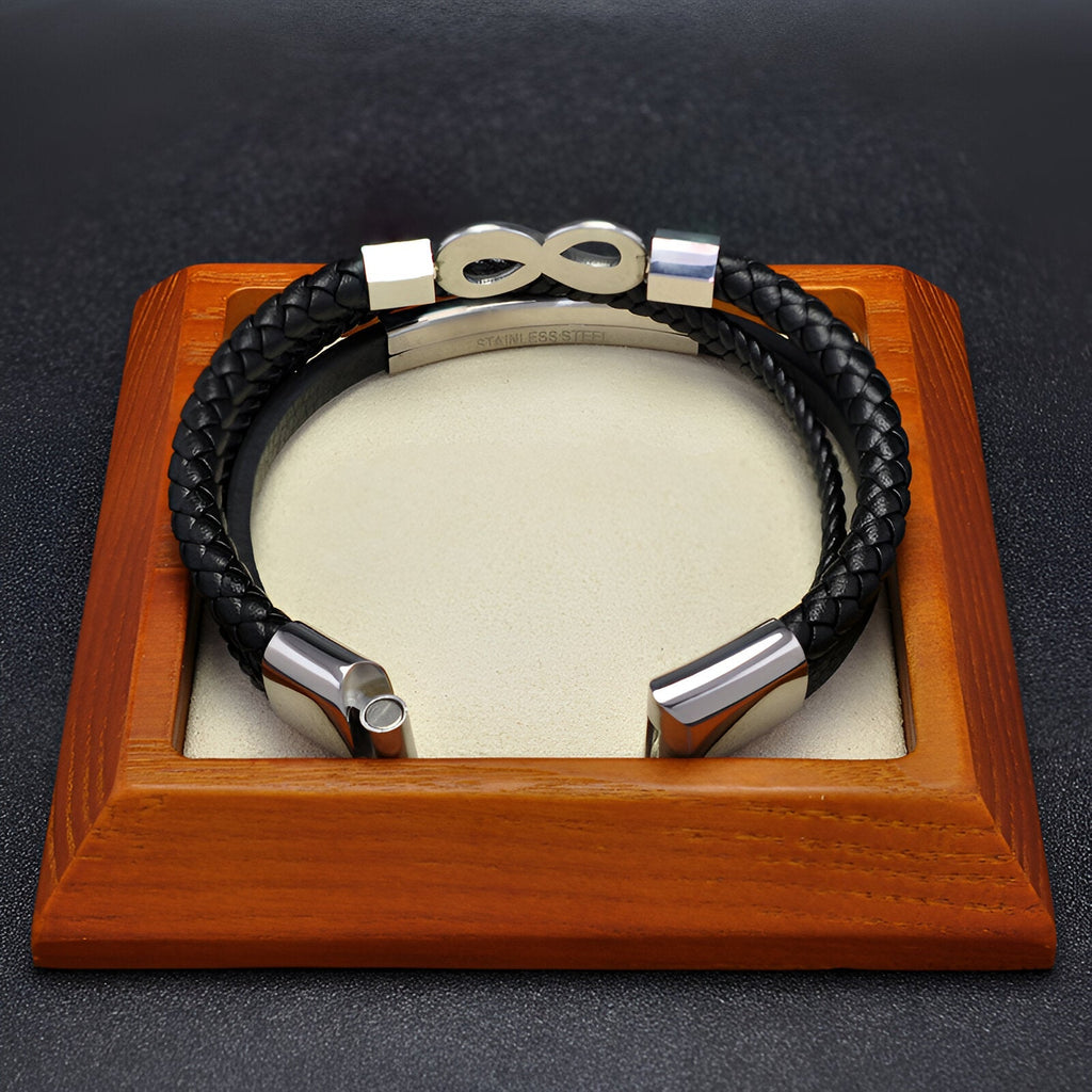 Bracelet multi-rangs en microfibre noire avec motif infini en métal argenté sur support en bois.