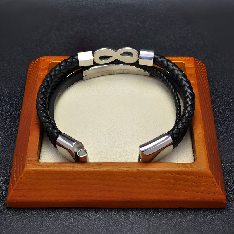 Bracelet multi-rangs en microfibre noire avec motif infini en métal argenté sur support en bois.