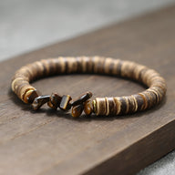 Bracelet homme en noix de coco brun avec perles et pierres naturelles œil de tigre sur bois.
