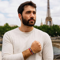 Bracelet en nylon tricolore rouge, blanc et bleu, style ajustable, porté au poignet homme devant la Tour Eiffel.
