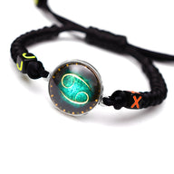 Bracelet en nylon noir tressé avec signe du zodiaque Cancer vert lumineux au centre, détails orange et jaune.