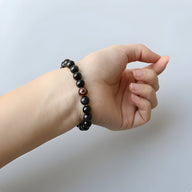 Bracelet mixte délicat en perles d’obsidienne arc-en-ciel noires avec perle rouge sur poignet clair.