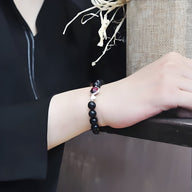 Bracelet noir en obsidienne avec perles en œil de tigre rose sur poignet, style mixte et élégant.