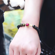 Bracelet mixte en perles noires d'obsidienne avec perles œil de tigre jaune et rose, charme central doré et rose.