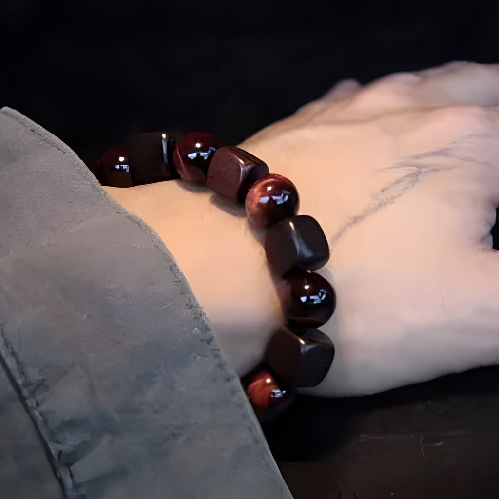 Bracelet mixte en perles d'œil de tigre rouge et bois d'ébène polies sur poignet clair.