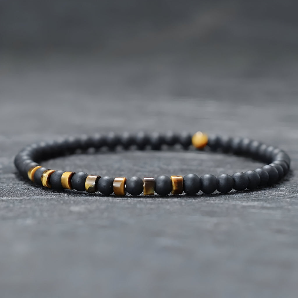 Bracelet fin pour homme en perles noires d'onyx avec accents métalliques et pierres jaunes œil de tigre.