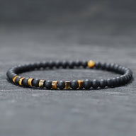 Bracelet fin pour homme en perles noires d'onyx avec accents métalliques et pierres jaunes œil de tigre.